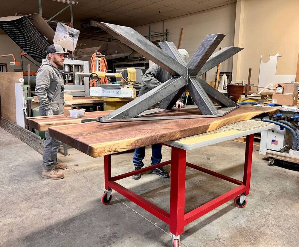 Two of the crew fitting a steel star base under a live-edge table top in the Denver shop